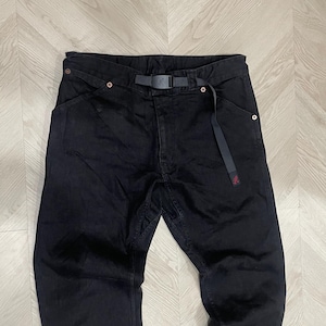 Puede incluir: Pantalones vaqueros negros con cintur&oacute;n negro incorporado. Los pantalones tienen un corte de pierna recta y un peque&ntilde;o logotipo rojo cerca del bolsillo derecho. Est&aacute;n colocados sobre una superficie de vetas de madera clara.