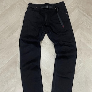 Puede incluir: Pantalones vaqueros negros con cintur&oacute;n negro incorporado. Los pantalones tienen un dise&ntilde;o de pierna recta y un detalle rojo en la trabilla del cintur&oacute;n. Se encuentran planos sobre una superficie clara con vetas de madera.