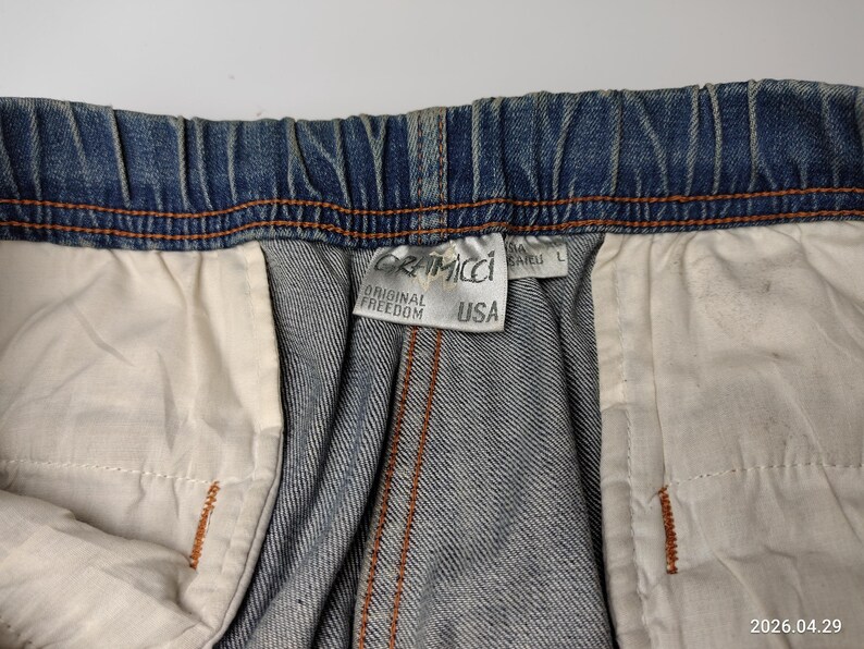 May include: Close-up of blue denim shorts with an elasticated waistband and orange stitching. The shorts have a white interior lining. A tag reads "Gramicci Original Freedom USA".
