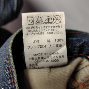 May include: Close-up of a tag on denim jeans. The tag includes washing instructions, fabric composition (100% cotton), and manufacturing details. The text is in Japanese and English.