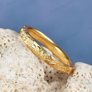 May include: A delicate gold band ring with a floral design. The ring is engraved with a repeating pattern of roses and leaves.
