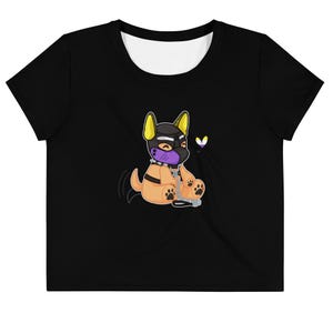 Peut inclure: Haut court noir avec un dessin de chiot de dessin animé. Le chiot porte un capuchon noir, un museau violet et un collier à chaîne. Il a une fourrure beige, des oreilles et des pattes jaunes. Un cœur du drapeau de la fierté non binaire flotte à proximité.