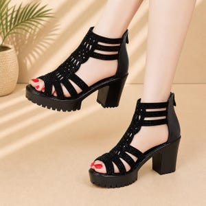 Op de afbeelding: Zwarte platformsandalen met een dikke hak. De sandalen met open teen hebben een decoratief ontwerp op de bovenkant met kleine versieringen. De sandalen hebben een ritssluiting aan de achterkant en een profielzool.