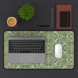 Op de afbeelding: Bovenaanzicht van een bureau met een groen en wit patroon muismat, een laptop en een witte muis. Een kopje koffie, een kleine plant en schrijfwaren zijn ook zichtbaar. Het bureau is donkergrijs.