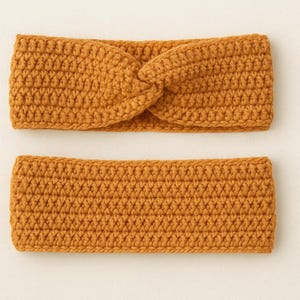 May include: Two mustard-coloured, crocheted headbands. One headband is a twisted style, and the other is a simple band. The headbands are made of a thick yarn and have a textured appearance. The headbands are displayed on a light beige background.