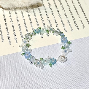 Könnte beinhalten: Eine zarte blaue und grüne Perlenblumenkrone mit einem Perlenakzent. Die Krone besteht aus kleinen Perlen und ist perfekt, um jedem Outfit einen Hauch von Verspieltheit zu verleihen.