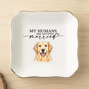 May include: A white ceramic trinket dish with a gold rim and a wavy edge. The dish features a watercolor illustration of a Golden Retriever and the text "MY HUMANS are getting married".