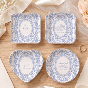 May include: Four ceramic trinket dishes with blue and white floral patterns and gold-toned rims. The dishes feature personalized text including initials L C, A L with 08.29.2026, t + s with 09.15.2026, and Andrew & Sarah with 11.05.2026, plus heart and hand icons.