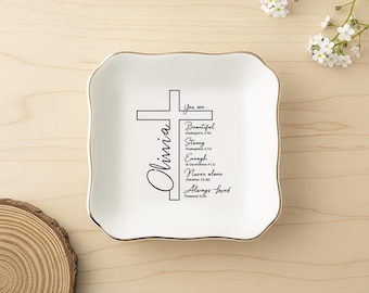 Op de afbeelding: Een vierkant wit keramieken schaaltje met een goudkleurige geschulpte rand. Het midden toont een zwart kruisontwerp met de naam Olivia en de tekst: You are Beautiful, Strong, Enough, Never alone, Always Loved, inclusief bijbelverzen.