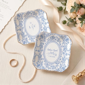 May include: Two square ceramic trinket dishes with scalloped edges and gold trim, featuring a blue and white floral pattern. One dish displays the letters L C, while the other shows the text Andrew & Sarah with a hand illustration and 11.05.2026.