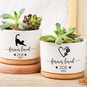 May include: Two white ceramic planters with succulents, each on a wooden base. One features a black cat silhouette, the other a heart with paw prints. Both read "forever loved," "ZOE," and "2025."