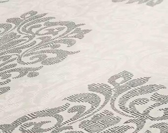 May include: Close-up of a cream textile with a repeating grey floral pattern. The design features stylised floral motifs with geometric details, creating a textured appearance. The fabric has a subtle sheen.