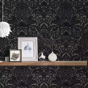Könnte beinhalten: Schwarz-graue Damasttapete mit sich wiederholendem floralem Muster. Ein Holzregal zeigt gerahmte Kunst, einen kleinen Ventilator, eine weiße Vase und einen dekorativen Behälter. Eine weiße, federartige Pendelleuchte hängt von der Decke.