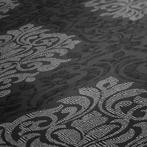 Könnte beinhalten: Nahaufnahme eines dunkelgrauen Stoffes mit einem sich wiederholenden, verzierten Muster. Das Design zeigt wirbelnde Blumen- und geometrische Formen in einem helleren Grau, wodurch ein subtiler Kontrast und ein strukturiertes Aussehen entstehen. Der Stoff hat einen leichten Glanz.