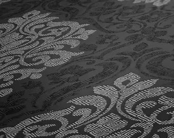 May include: A close-up shot of a dark gray fabric with a repeating, ornate pattern. The design features swirling floral and geometric shapes in a lighter gray, creating a subtle contrast and textured appearance. The fabric has a slight sheen.