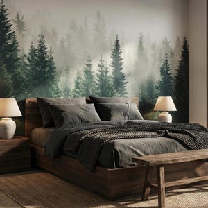 May include: A bedroom with a forest mural, a wooden bed frame, and matching nightstands. The bed is made with gray bedding and a knitted throw. Two lamps with cream-colored shades sit on the nightstands. A woven rug and a wooden bench complete the room.