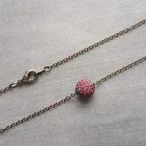 May include: A silver-toned necklace featuring a chain and a central, round pendant. The pendant is encrusted with small, vibrant pink stones. The necklace has a lobster clasp closure.