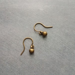 May include: Two antique brass-colored earring hooks with small, round beads. The earrings are displayed on a gray surface. The hooks are curved and have a simple, elegant design, perfect for jewelry making.