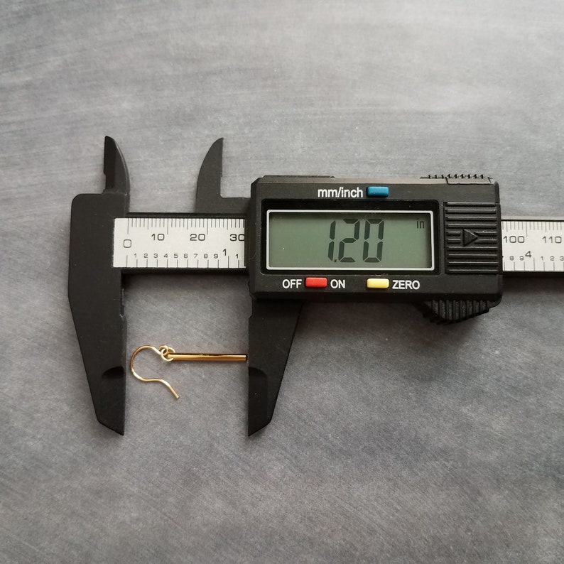 Peut inclure: Une boucle d'oreille dor&eacute;e avec un crochet est mesur&eacute;e avec un pied &agrave; coulisse num&eacute;rique. Le pied &agrave; coulisse affiche une mesure de 3,05 cm. La boucle d'oreille est pos&eacute;e sur une surface grise.