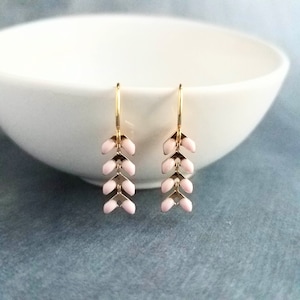 May include: A pair of gold-colored earrings with a delicate, leaf-like design. Each earring features a series of light pink, petal-shaped elements connected by gold-toned metal. The earrings hang from a simple gold hook.