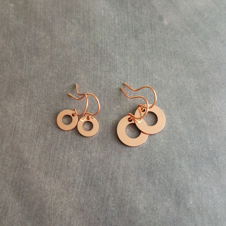 May include: Two pairs of copper-colored earrings. Each earring features a small, open circle design. The earrings are displayed on a gray surface. The earrings are lightweight and suitable for everyday wear.