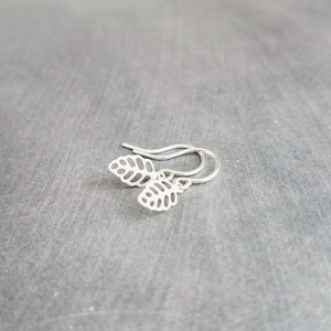 May include: A pair of silver leaf earrings. Each earring has two openwork leaf charms suspended from a simple ear wire. The leaves have a detailed vein pattern, and the earrings are displayed on a grey surface.