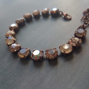 May include: A close-up of a bracelet featuring iridescent, round gemstones set in a bronze-colored metal. The gemstones have a range of colors, including gold, peach, and hints of blue. The bracelet is on a dark gray surface.
