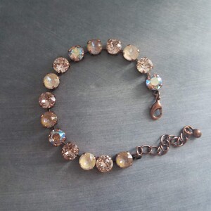 May include: A delicate bracelet featuring a series of round, iridescent crystals in shades of champagne and peach. The crystals are set in a copper-toned metal, connected by a chain and clasp. The bracelet is designed to be worn around the wrist.