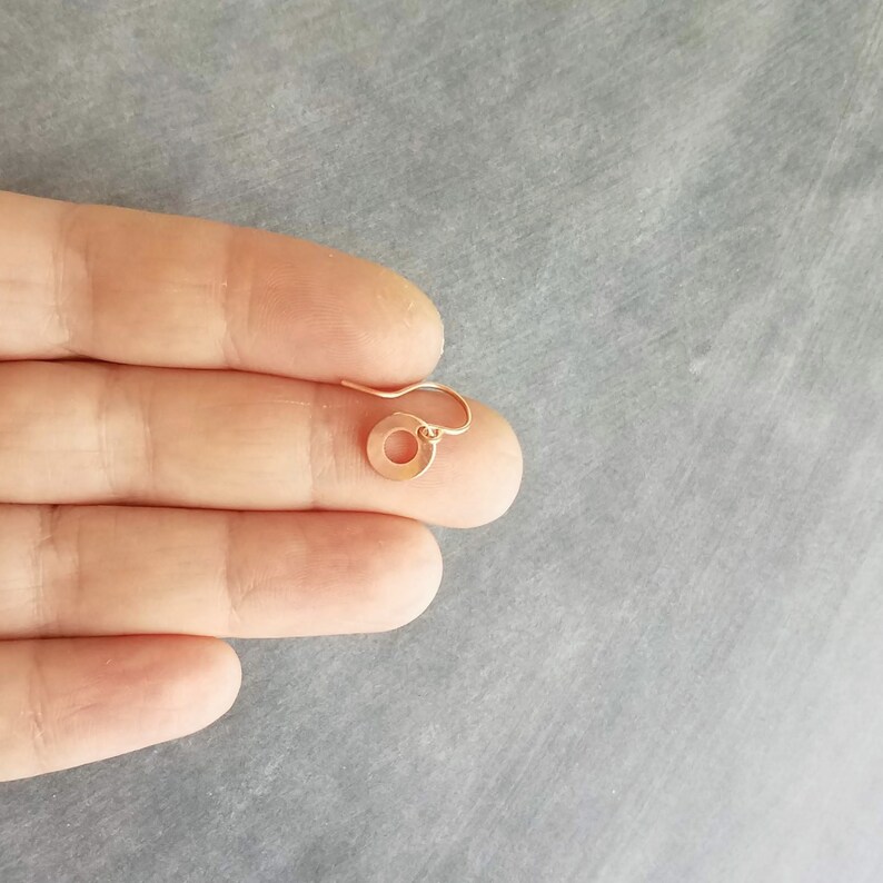 May include: A single, small, gold-colored earring with a circular pendant and a hook. The earring is shown against a gray background.