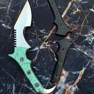May include: A custom karambit knife with a mint green handle and a silver blade. The handle has a geometric pattern and is secured with silver screws. Two black handle scales and a small hex key are also present.