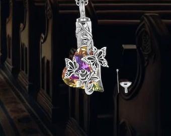 May include: Silver heart-shaped cremation necklace with a butterfly design and colorful crystals. The necklace comes with a small funnel for filling the pendant.