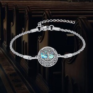 May include: Silver bracelet with a circular pendant depicting a tree of life. The pendant has a blue and green iridescent inlay and Celtic knot detailing. The bracelet has a fine chain and a lobster clasp. The overall design is intricate.