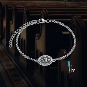 May include: Silver-toned bracelet featuring an oval pendant with a floral design. The bracelet has a delicate chain and a secure clasp. Includes small tools for adjustment. The background is blurred, suggesting a church setting.