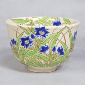 May include: A white ceramic bowl with a floral design. The bowl is decorated with blue and green flowers and leaves on a white background.