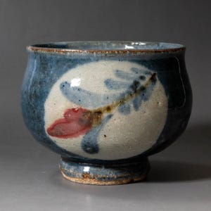 Peut inclure: Bol en céramique fait à la main, extérieur bleu et motif central blanc. Le blanc présente un motif floral rouge et bleu. Le bol est de forme arrondie et possède une petite base robuste, idéal pour servir ou décorer.