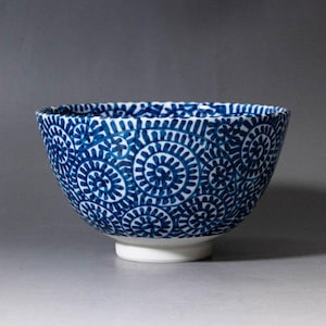 May include: A ceramic bowl with a white base and a blue spiral pattern. The bowl's interior and exterior are decorated with a repeating design of blue spirals on a white background. The bowl is a decorative item.