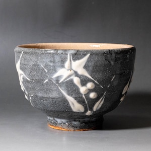 Pode incluir: Uma tigela de cerâmica com um exterior texturizado cinzento-escuro com motivos florais e de bagas pintados à mão em branco. O interior da tigela é de uma cor bege clara e lisa, e a base é de um material de argila laranja-acastanhado.