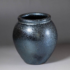 以下が含まれることがあります： 濃い青色の陶器の花瓶で、まだらで質感のある表面です。花瓶は丸みを帯びたボディと広い開口部を持っています。まだらの模様は上部に集中し、底に向かって薄くなっています。花瓶はおそらく手作りです。