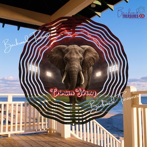 May include: A decorative metal wind spinner featuring an elephant in a stadium with the text "Crimson Strong." The design incorporates red and white stripes, with the words "Backroad Treasures" in a cursive font.