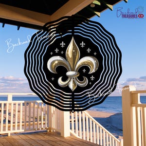 May include: A black and gold fleur-de-lis wind spinner with a wavy border. The fleur-de-lis is gold with white accents, set against a black background. The spinner is hanging on a porch overlooking the ocean.