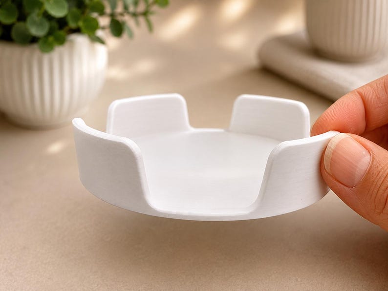 Pu&ograve; includere: Un supporto circolare in plastica bianca con una base piatta e quattro linguette verticali equidistanti che si estendono verso l'alto dal bordo. L'oggetto presenta una finitura opaca liscia e un design semplice e funzionale.