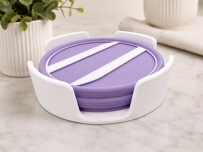 Pu&ograve; includere: Una pila di sottobicchieri rotondi viola con strisce diagonali bianche, tenuti all'interno di un supporto circolare bianco. I sottobicchieri presentano una superficie liscia e piatta con un bordo rialzato e il supporto ha quattro sostegni curvi.