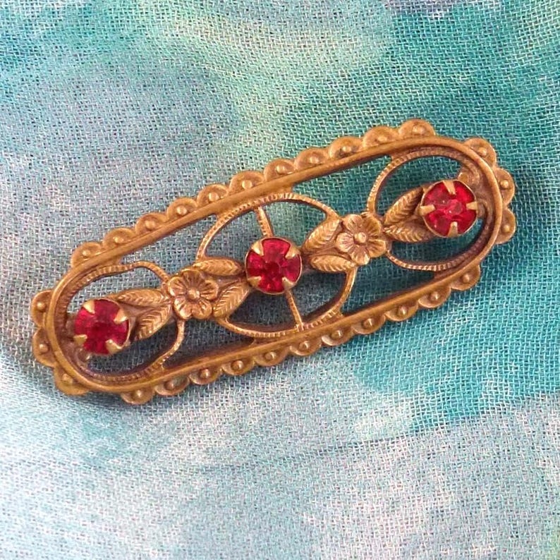 A gold tone bar pin with a floral setting and red rhinestones