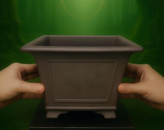 May include: A dark brown, square bonsai pot with a rectangular design on the front. The pot is held by two hands, and sits on a black stand. The background is a blurred green forest scene.