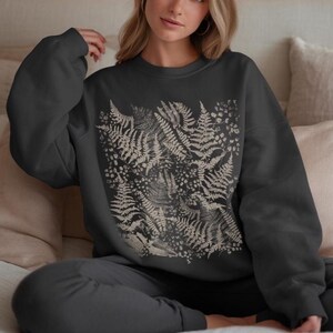Puede incluir: Sudadera gris oscuro y pantal&oacute;n a juego. La sudadera presenta un estampado beige de helechos y flores en la parte delantera. El conjunto es c&oacute;modo e informal, adecuado para el uso diario. El dise&ntilde;o est&aacute; inspirado en la naturaleza.