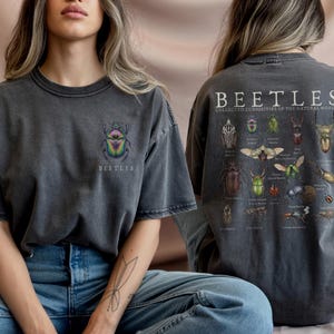 Peut inclure: T-shirt gris foncé avec un motif de coléoptère coloré sur le devant et une illustration détaillée d'insectes au dos. Le texte "BEETLES" et "COLLECTED CURIOSITÉS DE LA NATURE" sont imprimés.