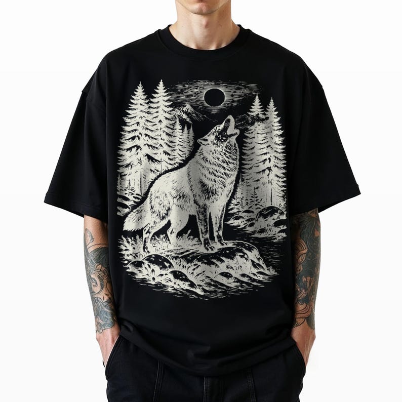 Puede incluir: Una camiseta negra de manga corta con un estampado gr&aacute;fico blanco de un lobo aullando a la luna llena. La escena incluye un denso bosque de pinos y terreno rocoso, representados en un estilo ilustrativo detallado y de alto contraste.