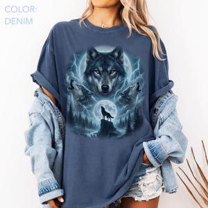 K&ouml;nnte beinhalten: Denimblaues T-Shirt mit Wolfsmotiv. Die Grafik zeigt ein zentrales Wolfsgesicht, drei heulende W&ouml;lfe, einen Vollmond und Blitze. Der Text "COLOR: DENIM" ist oben links sichtbar.
