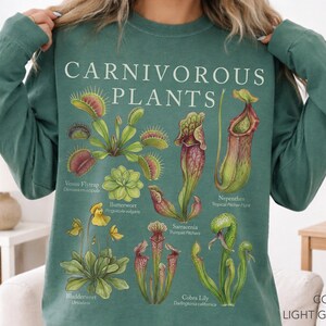 Puede incluir: Una sudadera de manga larga de color verde claro con una ilustración botánica de varias plantas carnívoras, incluyendo Venus atrapamoscas, Pinguicula, Nepenthes, Sarracenia, Utricularia y Darlingtonia, con el texto "CARNIVOROUS PLANTS" impreso.