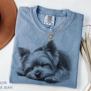 Puede incluir: Camiseta azul vaquero con una ilustraci&oacute;n detallada de un Yorkshire Terrier durmiendo. La camiseta tiene cuello redondo y mangas cortas. Un collar de oro con un colgante descansa sobre la camiseta. La etiqueta dice "Comfort Colors".